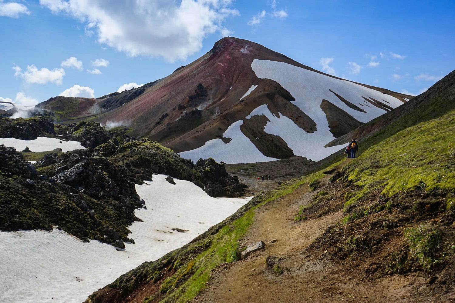 Hikers wandering between colorful mountains with snow, moss and steam patches