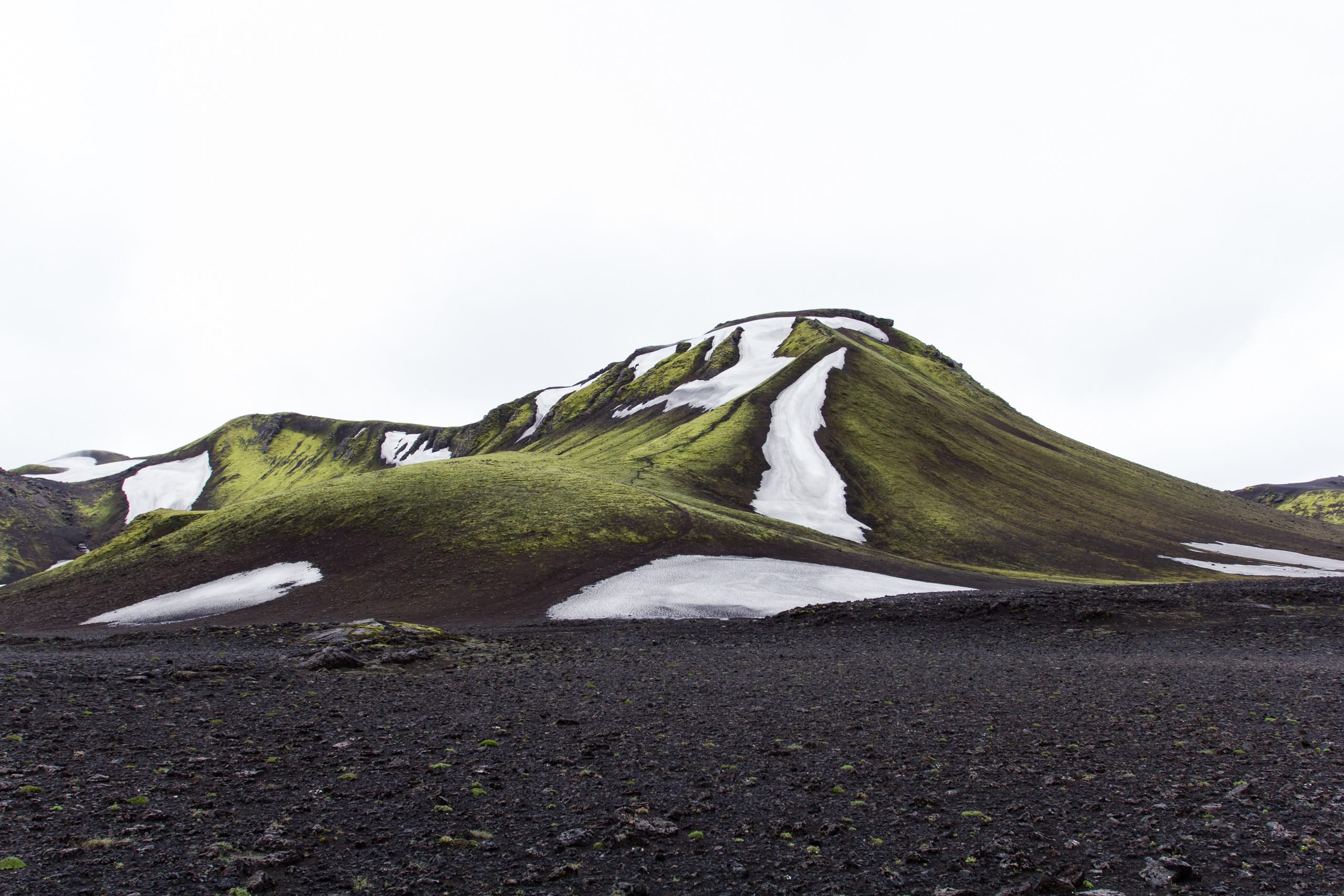 Peaky, moss covered mountain rises over the black desert